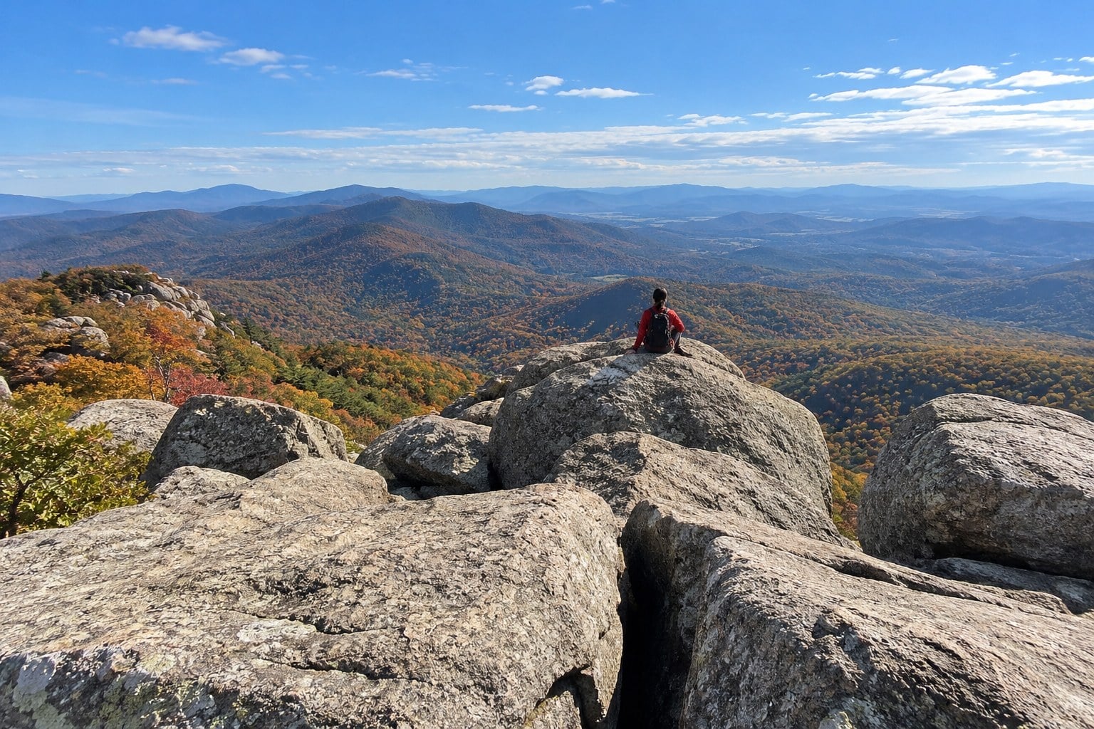 Hiker resting on the granite summit of Old Rag above fall color