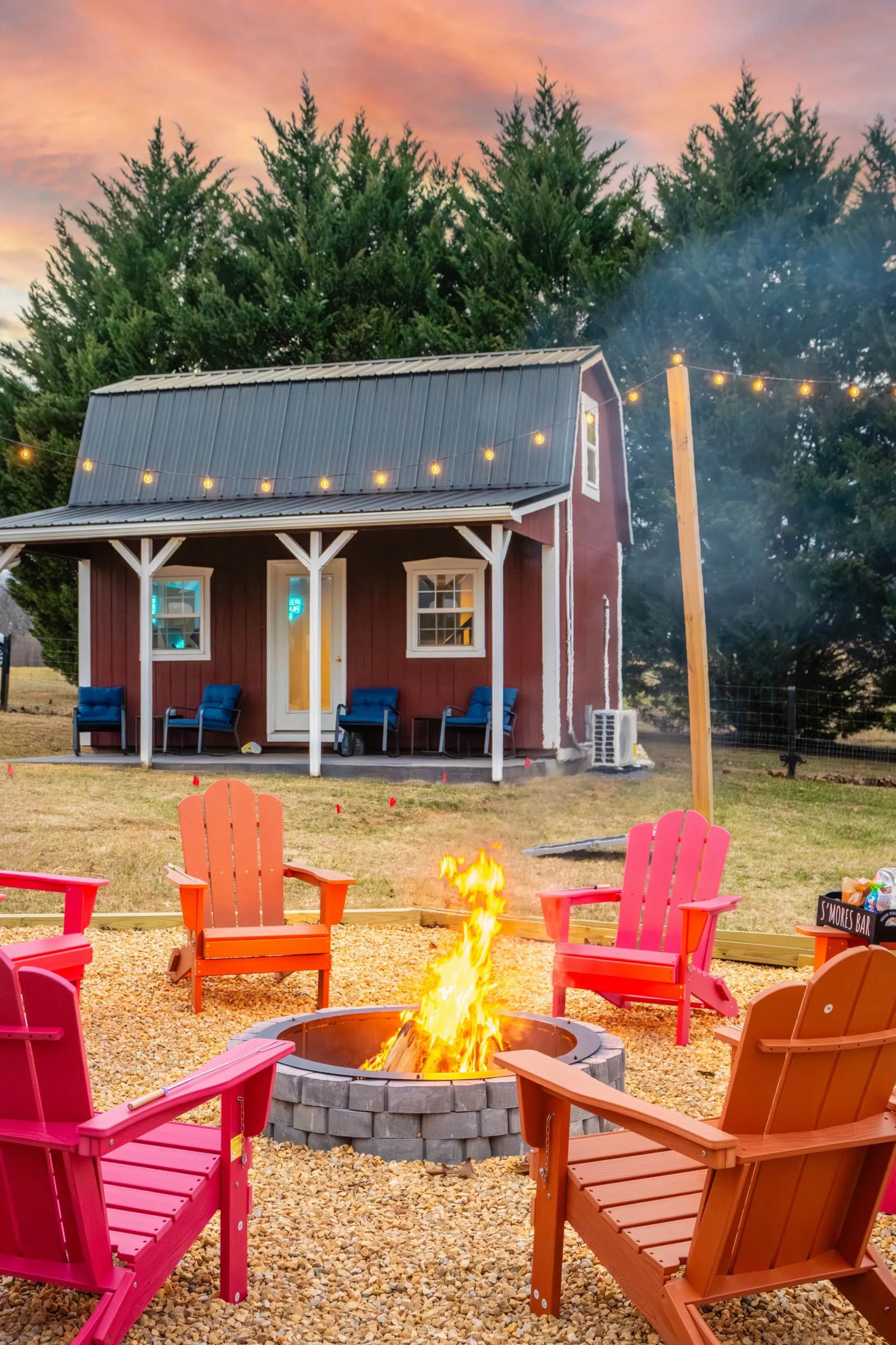 Red barn-style cottage at sunset with string lights and a fire pit ringed by Adirondack chairs in Luray, VA