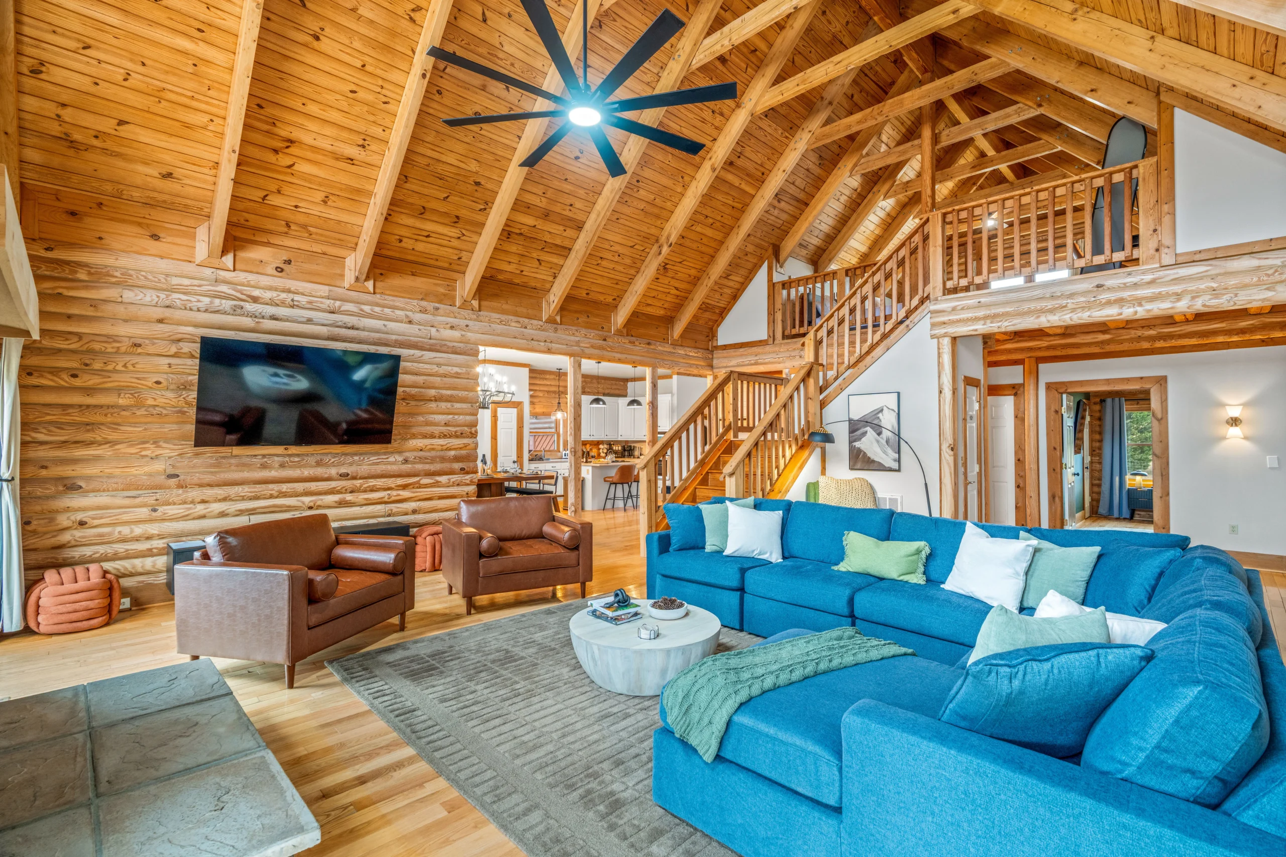 Living room with blue sectional sofa, exposed wood beams, and loft stairs in a Luray VA short-term rental