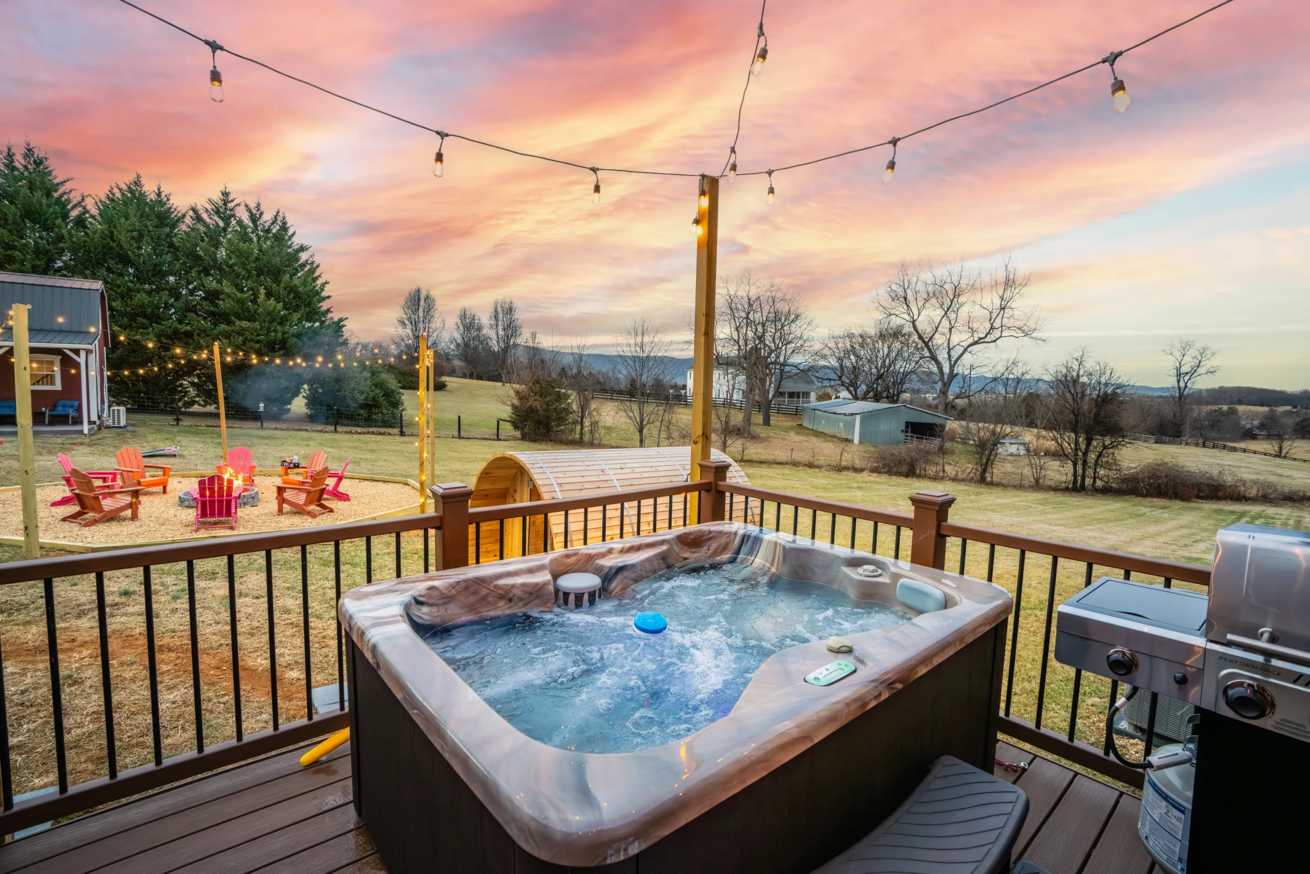 Private hot tub on the deck at Skyline Vista Retreat at dusk, with string lights overhead and lawn chairs
