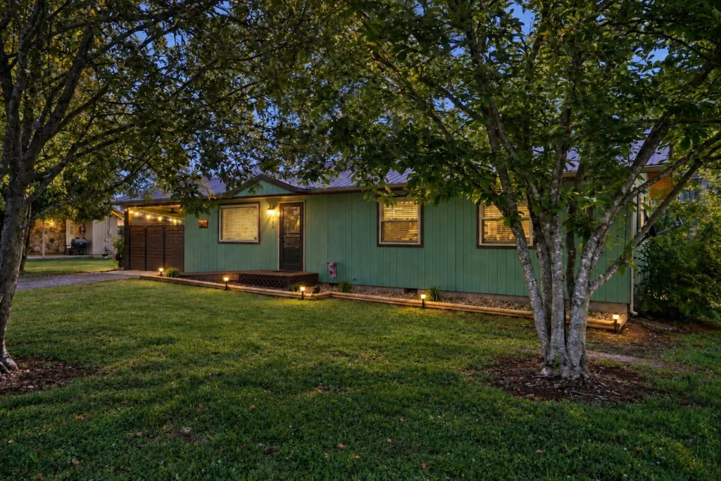 Green cottage exterior at dusk with warm lighting and shade trees, a shenandoah national park cabins stay from Endless Stays