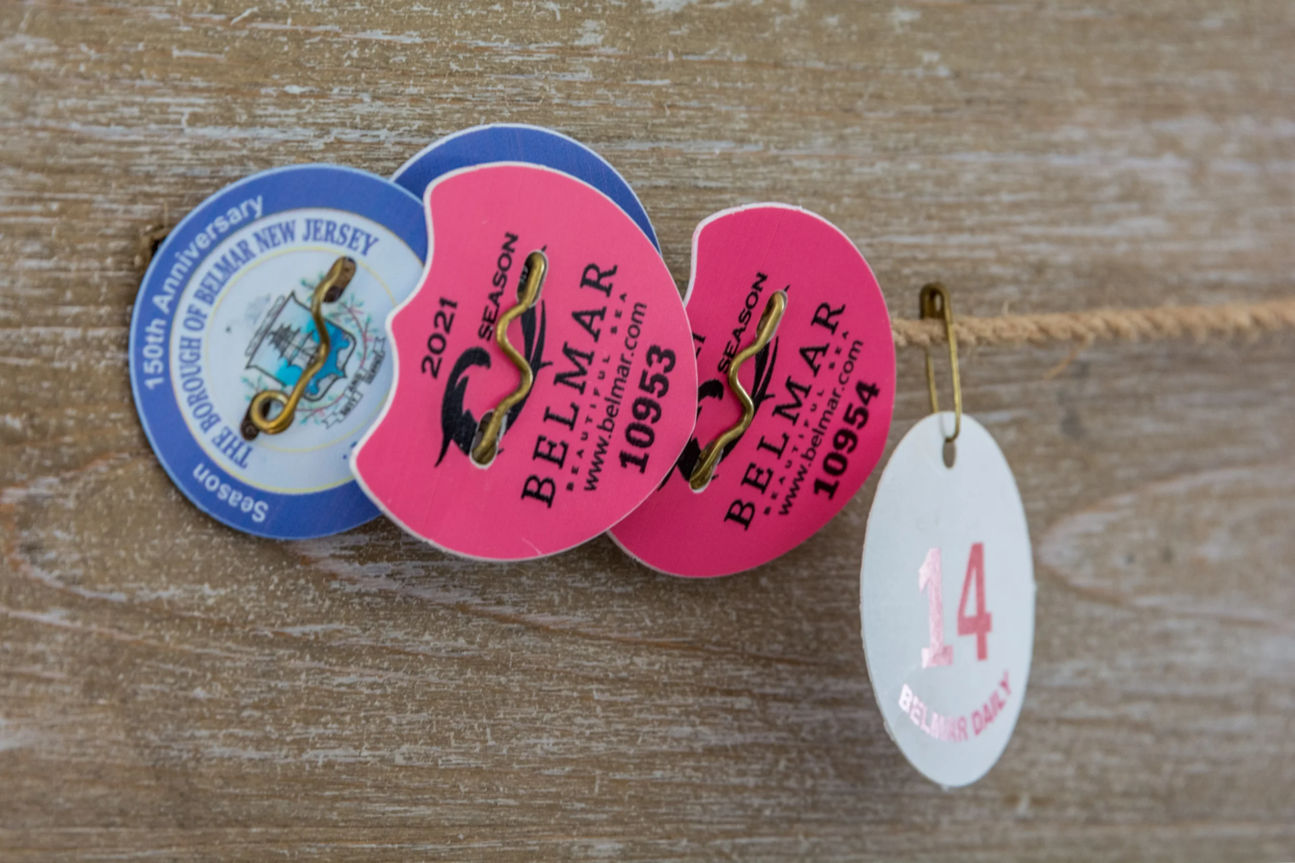 Vintage Belmar NJ motel key tags on weathered wood, including a blue and white 150th Anniversary tag and pink 2021 season