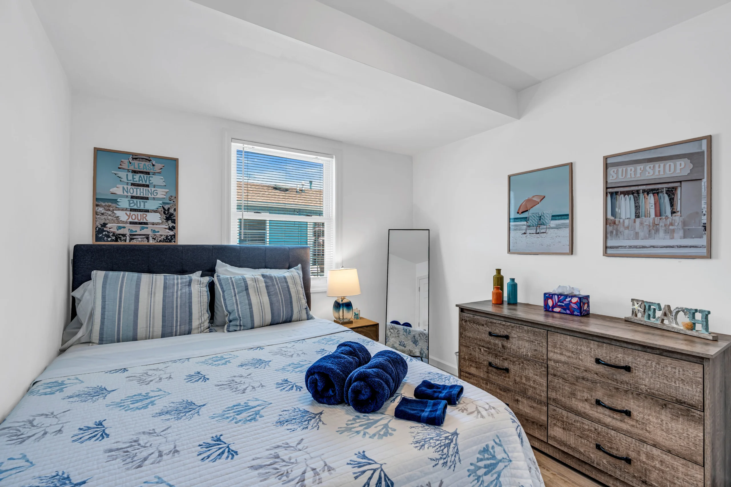 Bright coastal bedroom with coral-print blue and white bedding and ocean views through blue shutters, a turnover cleaning