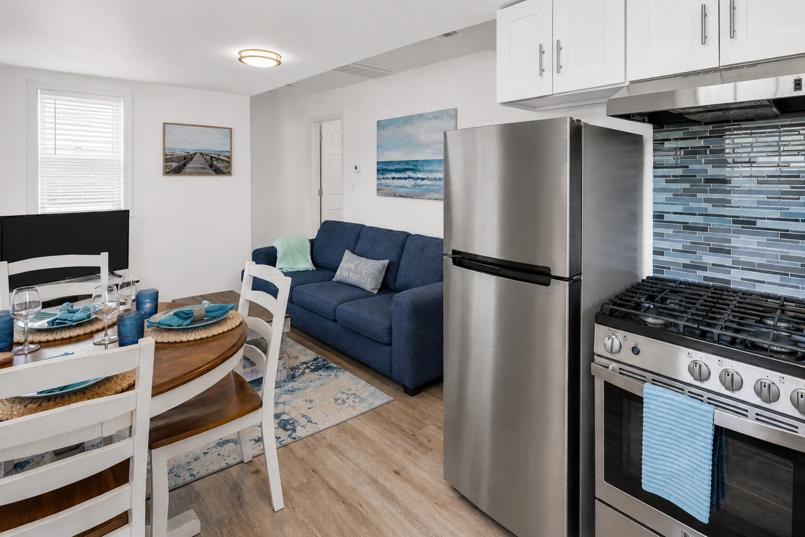 Open-concept kitchen with white cabinets and blue mosaic backsplash beside a navy sofa, a Belmar NJ Airbnb rental for net