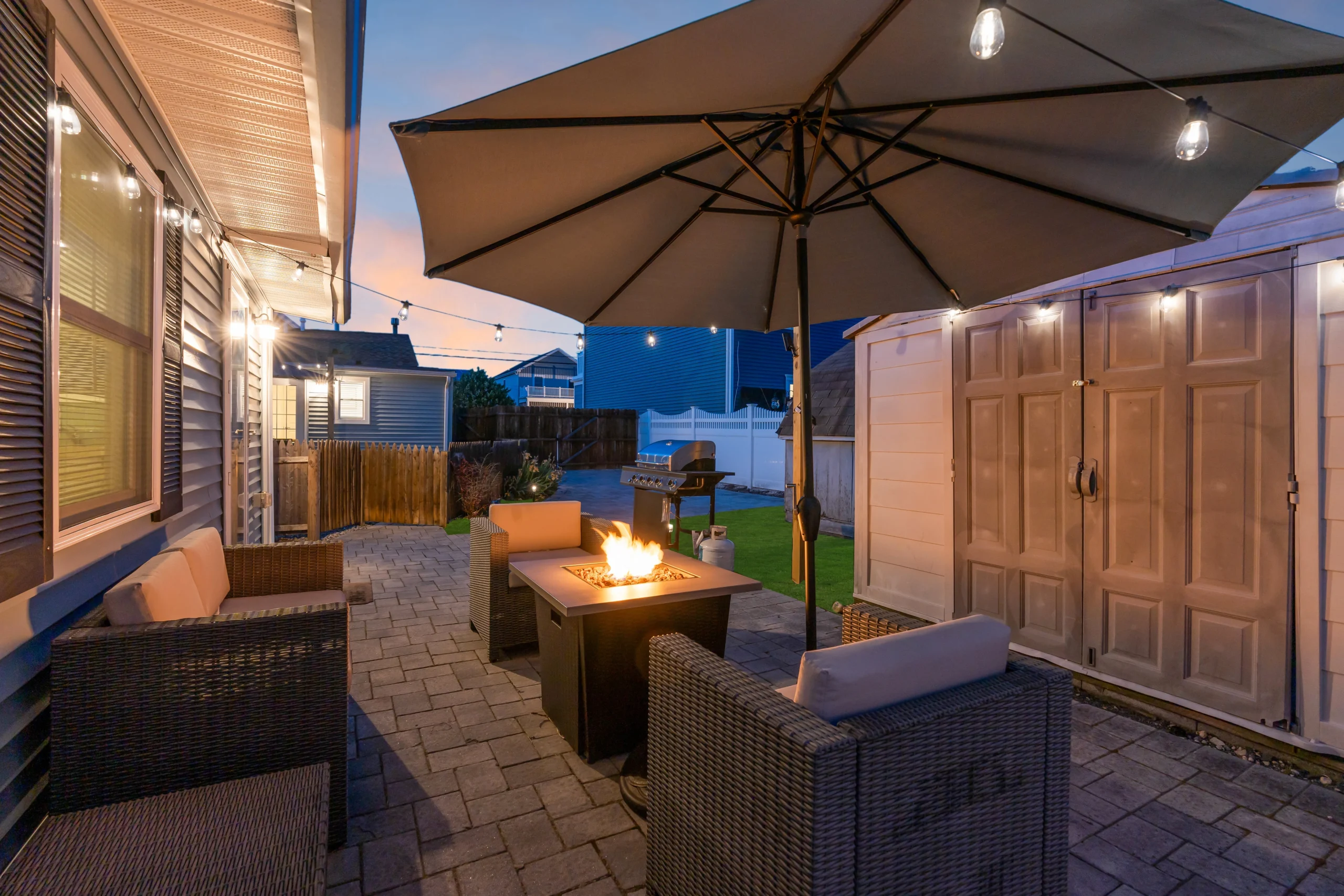 Modern backyard patio with fire pit, wicker seating, and ocean views at twilight in Belmar