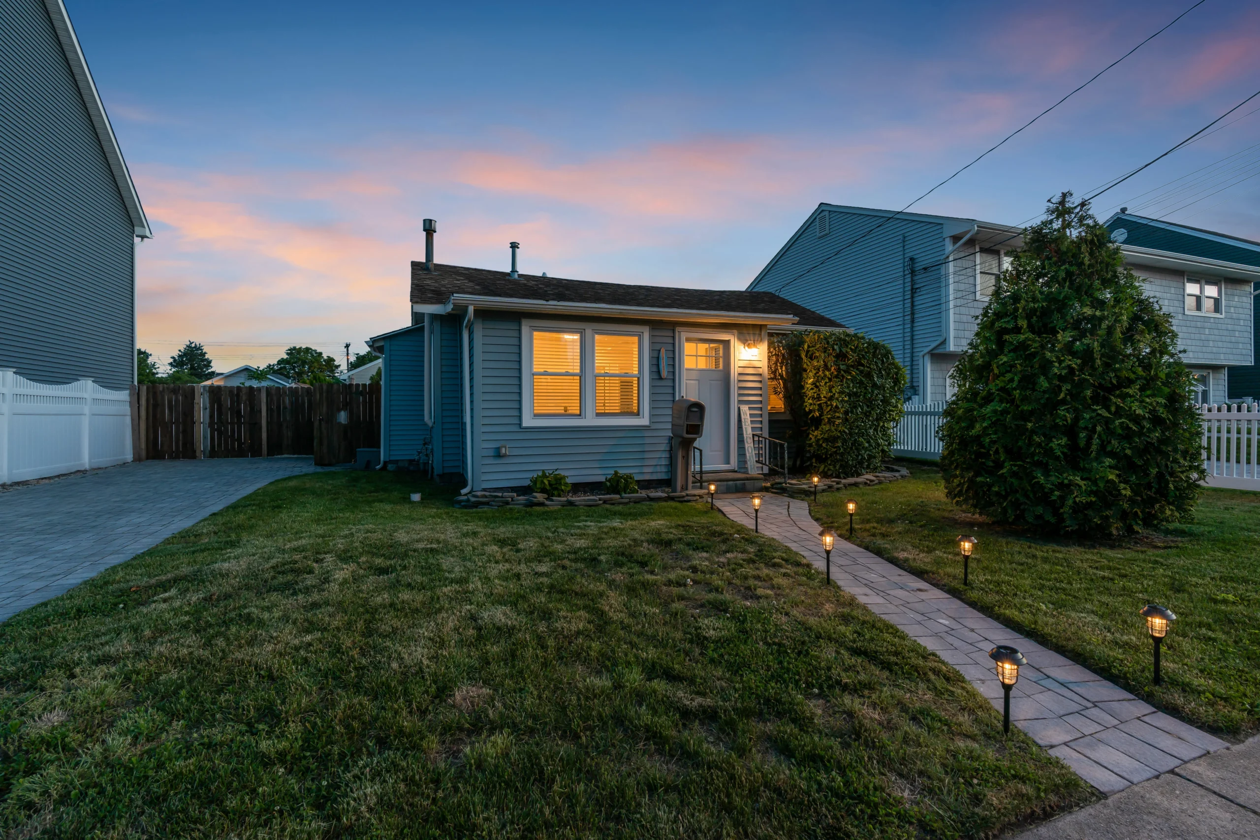 Blue cottage with illuminated windows and pathway lighting in Belmar summer rental property