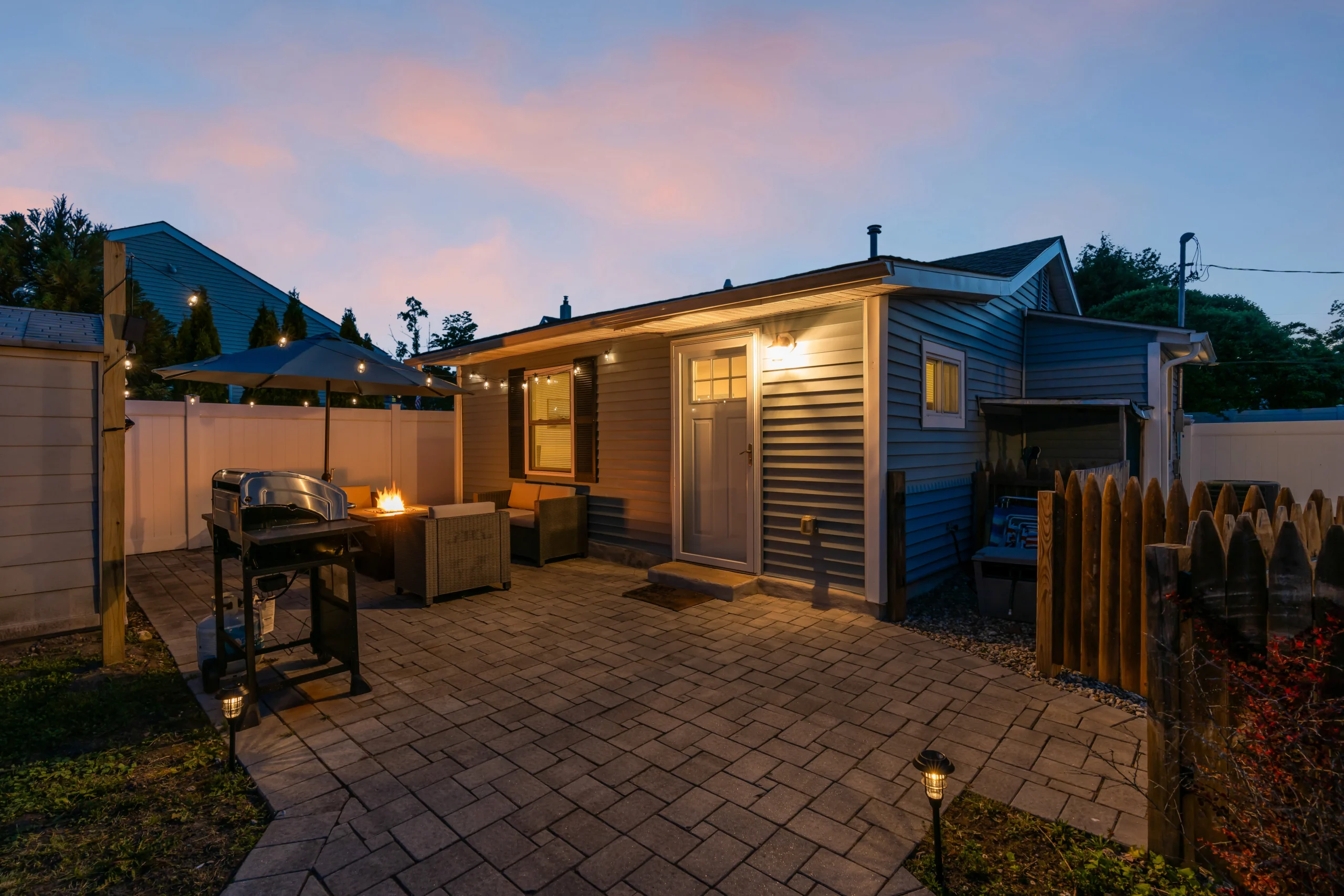 Twilight patio with fire pit and built-in seating beside blue-sided cottages at The Belmar Family Compound, a Blue