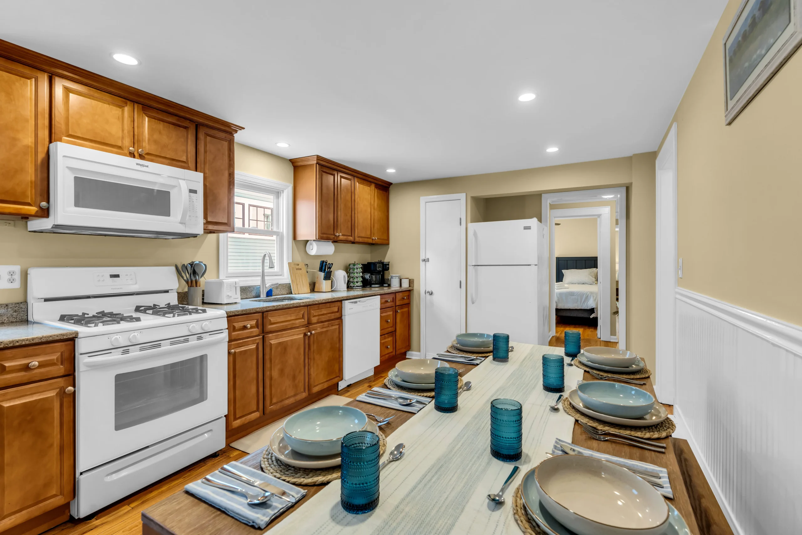 Kitchen dining area with wood cabinets, granite counters, yellow accent wall, and a set table in a Bradley Beach, NJ Airbnb