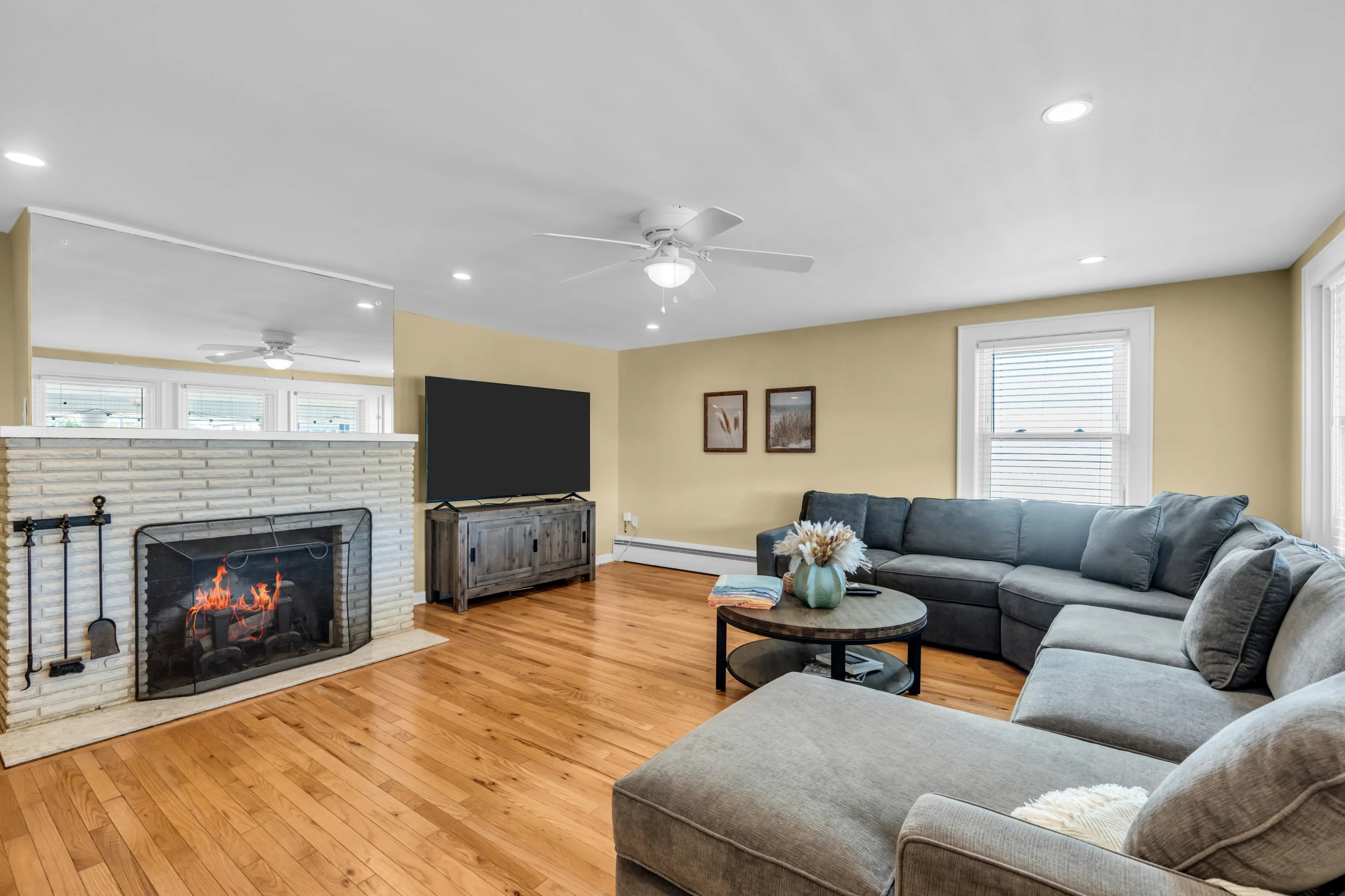 Living room with warm yellow walls, hardwood floors, and lit white brick fireplace, a summer Airbnb rental in Bradley Beach,