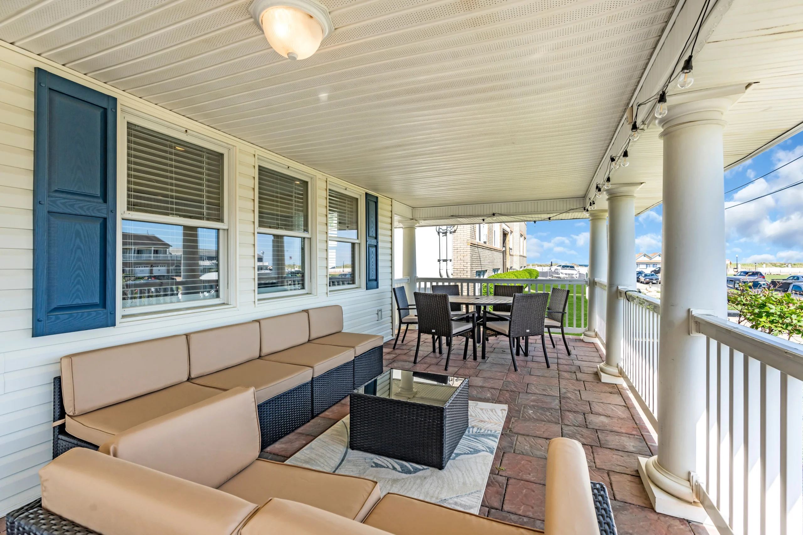 Covered patio with tan and black wicker seating and a dining table overlooking the coast at our client home in Bradley Beach