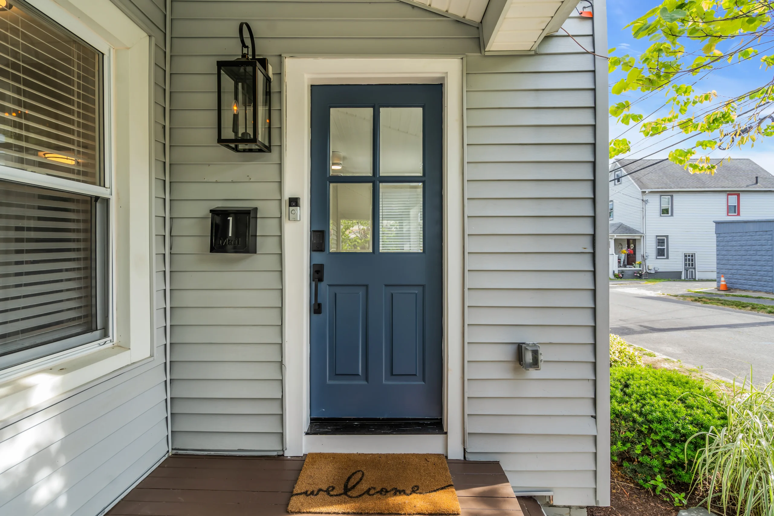 Modern coastal home entrance with blue paneled door and lantern sconce at Ocean Grove vacation rental