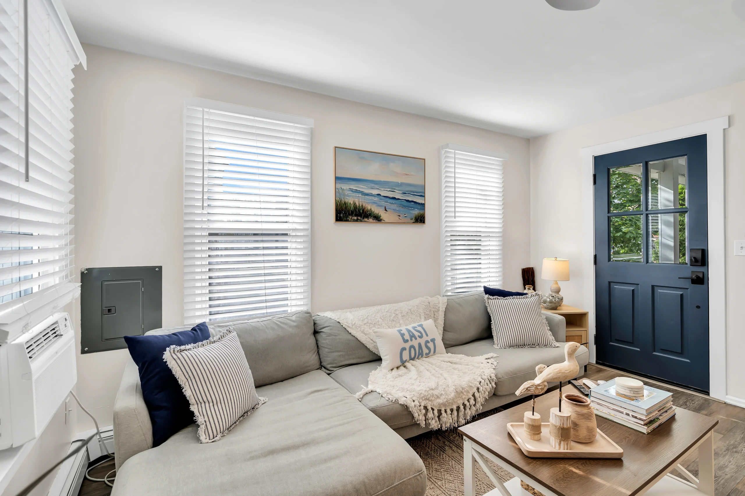 Bright coastal living room with gray sectional sofa and beach decor, a guide to reviewing gross vs net Airbnb income in