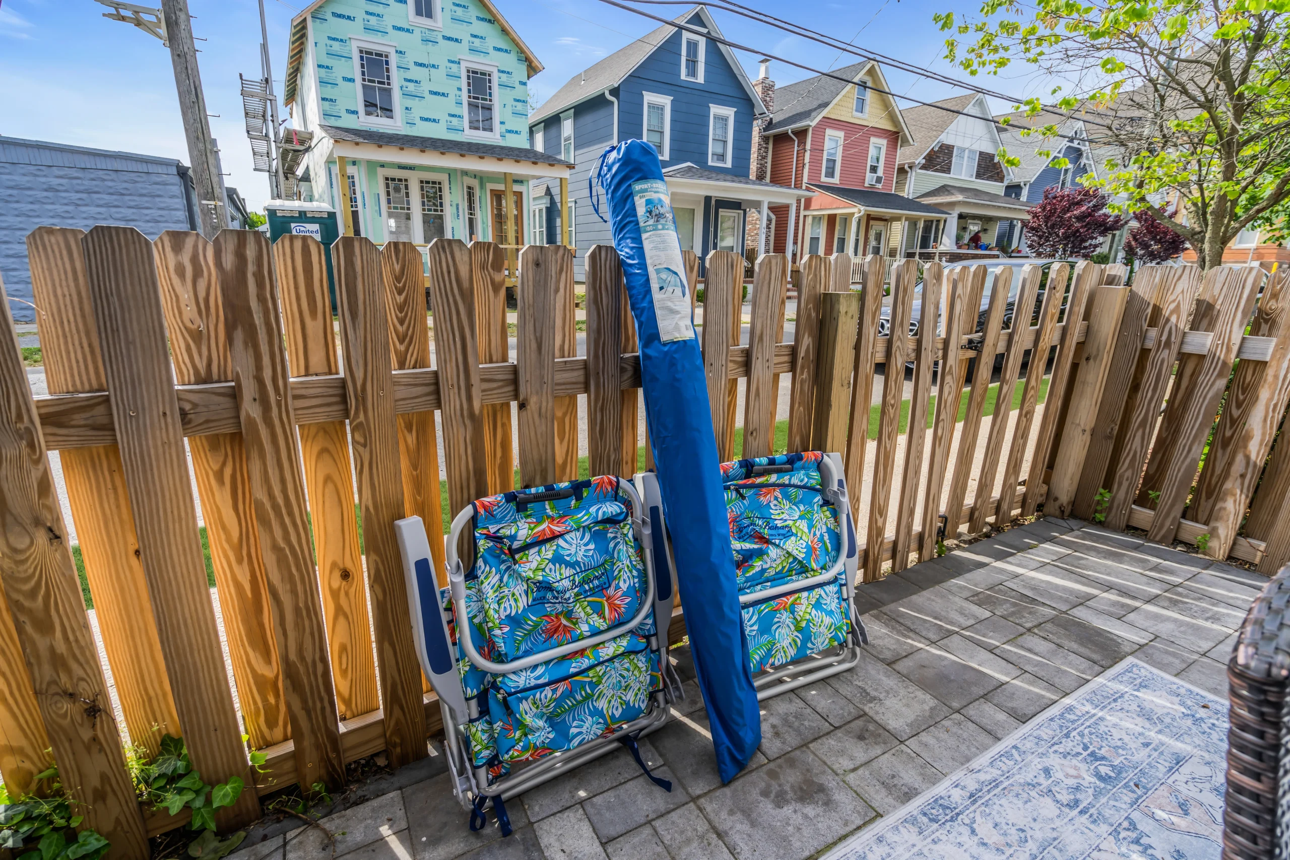 Beach house patio with weathered wood privacy fence, blue raft and tropical-print beach chairs, Ocean Grove NJ Airbnb rental